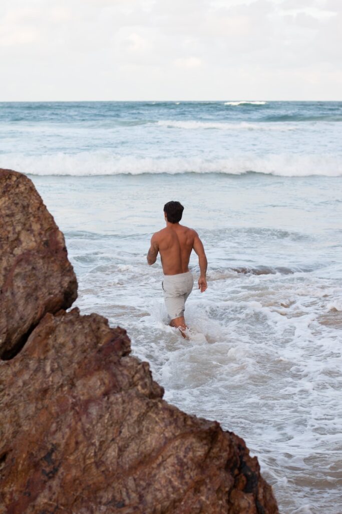 a man walking out of the ocean with a surfboard