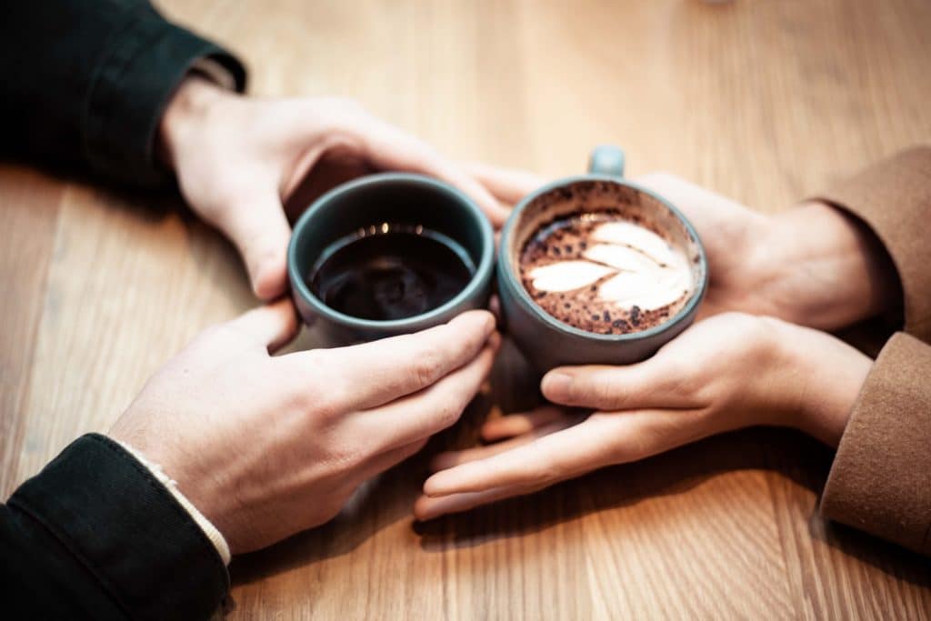 trouver le Grand Amour: 2 mains d'un homme tenant un café et 2 mains d'une femme tenan tun cappuccino