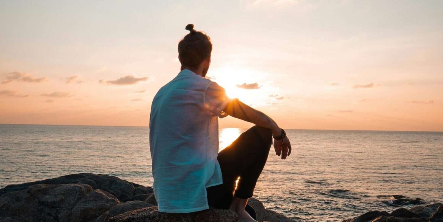 a man sitting on a rock looking at the sunset