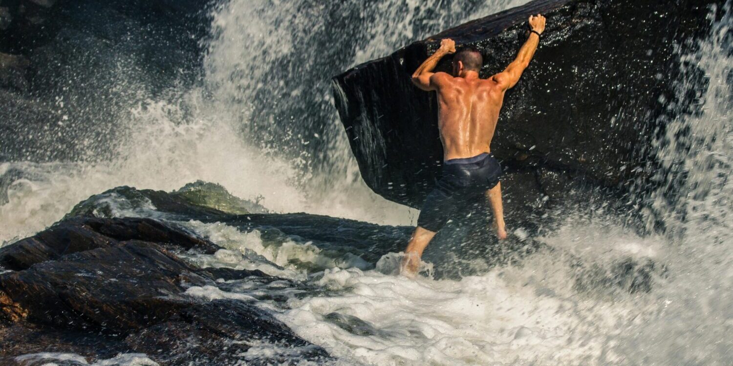 a man climbing a rock in a waterfall